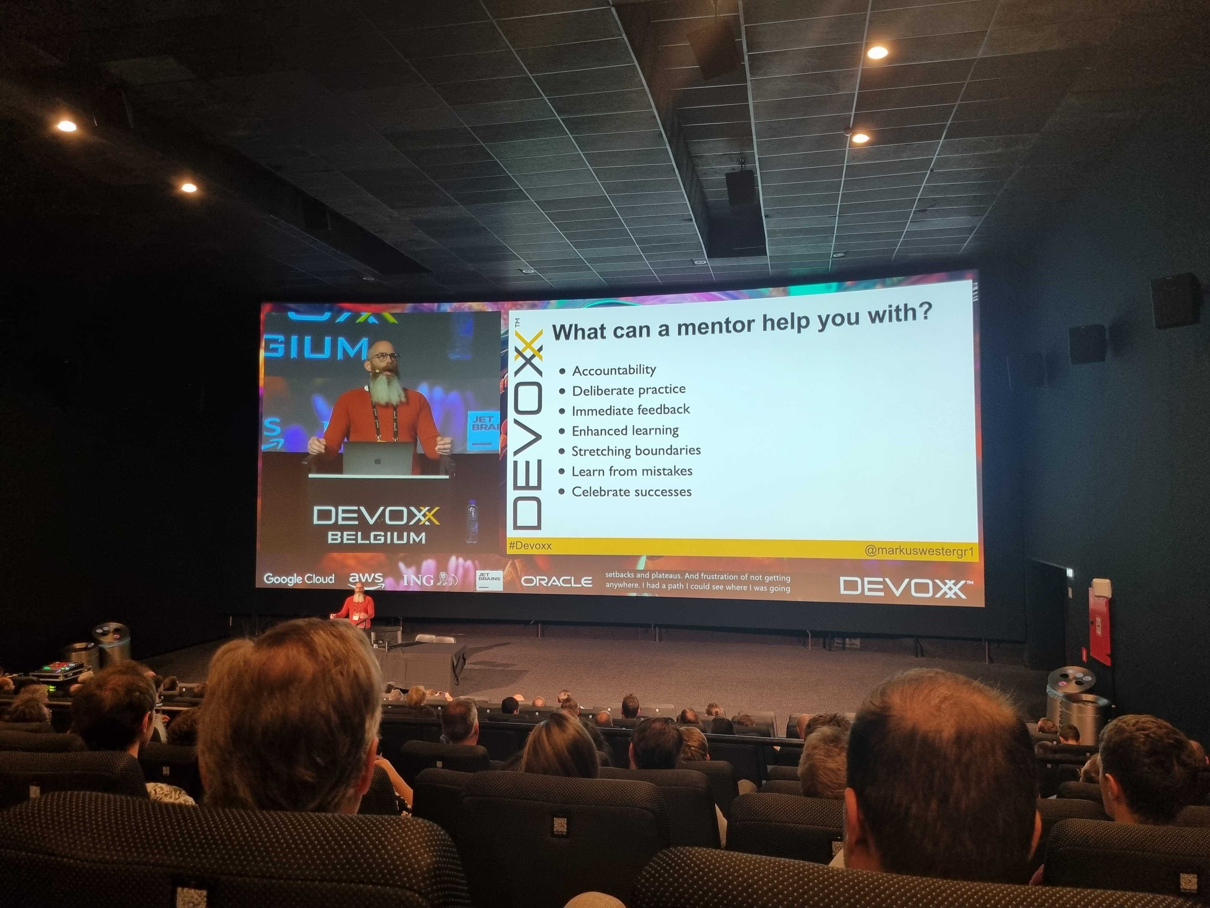 A presenter behind podium with slide titling What can a mentor help you with?.